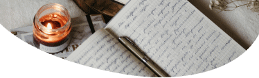 Image of an open book with handwriting and a pen lying along the center fold