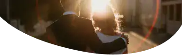 The back of a man and a woman standing together and looking into the sunset. and he has his arm around her shoulder