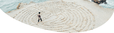 Image of a person standing on a beach walking through a maze made of lines on the sand