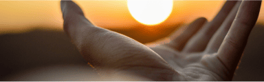 A hand reaching out towards the orange sky, as if holding the setting sun