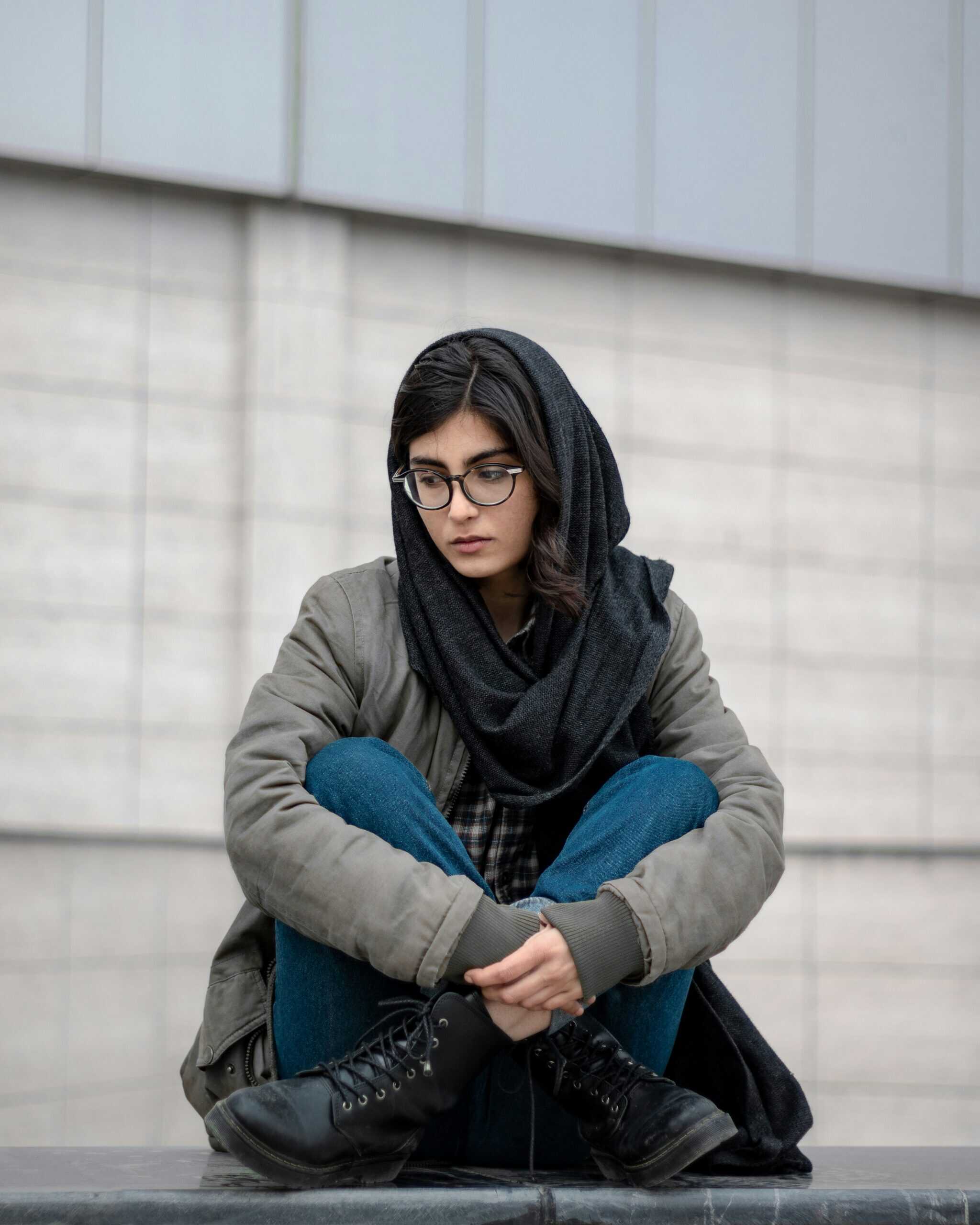 A young Muslim girl wearing a scarf loosely around her head and casual clothing and looking deep in thought